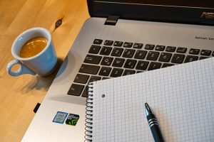 stanowisko pracy zdalnej - laptop, notes z długopisem, kawa, biurko